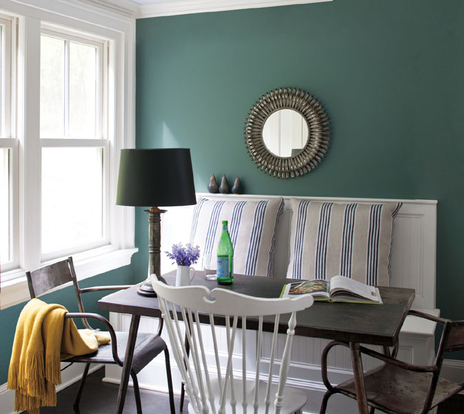 A dining room with Caribbean Teal 2123-10 walls and a large window painted in Chantilly Lace 2121-70. The room is styled with a white wooden bench and mis-matched chairs.