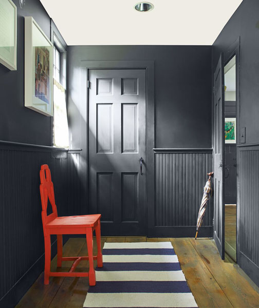 A mono-chromatic hallway with walls, woodwork, doors and panelling painted in Soot 2129-20. A vibrant chair painted in Tomato Red 2010-10 provides an unexpected pop of red.