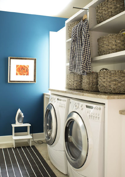 A laundry room with an accent wall painted in Blue Danube 2062-30.  Open shelving is painted in Cloud White OC-130 and styled with wicker baskets.