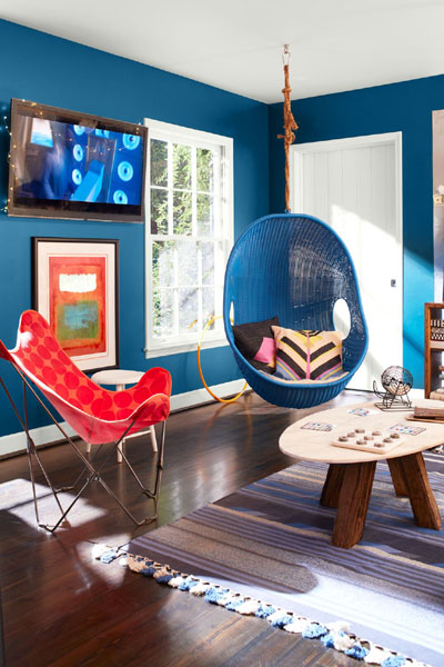 An informal sitting room with hanging blue wicker chair, red polka dot fabric chair and striped rug.  The walls are painted in Bermuda Blue 2061-30 and the woodwork is painted in White Heron OC-57.