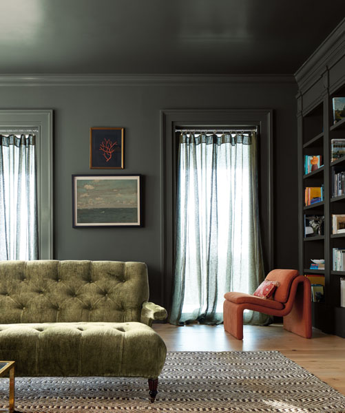 A library colour-drenched in Ashwood Moss 1484. The room is styled with a geometric rug, burnt orange occasional chair and button-back sofa.