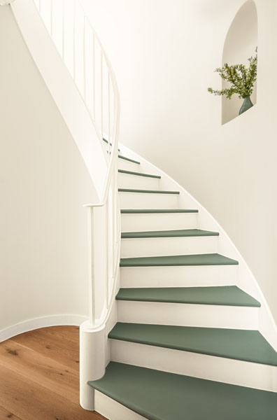 A curved stairway with walls painted in Sea Salt CSP-95 and stair treads painted in Rosepine 461. A floral arrangement decorates the curved alcove.