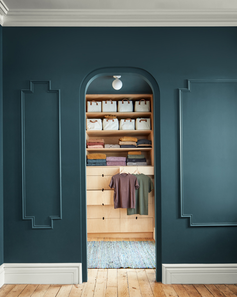 A view through an arched doorway into a walk-in wardrobe. The outer panelled walls are painted in Stained Glass CSP-685 and the woodwork and ceiling are painted in Glacier White OC-37.