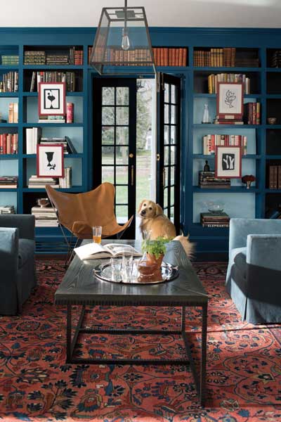 A painted wall to ceiling bookcase with outer faces painted in Lucerne AF-530 and inner faces painter in Exhale AF-515. The room features a patterned rug and armchairs